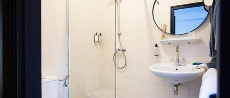 Un baño moderno con cabina de ducha de vidrio, inodoro blanco y lavamanos con espejo arriba.