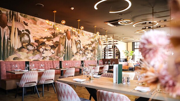 Interior de un restaurante con un mural, iluminación moderna y una zona de bar.
