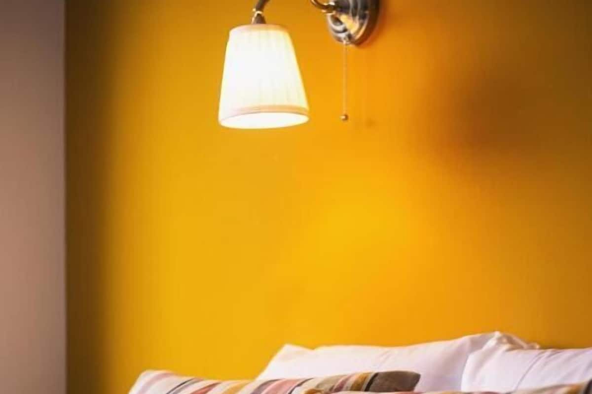 Una cama con almohadas a rayas y una lámpara en la pared.
