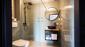Un baño moderno con cabina de ducha de vidrio, inodoro blanco, espejo redondo y lavamanos con lavabo negro.