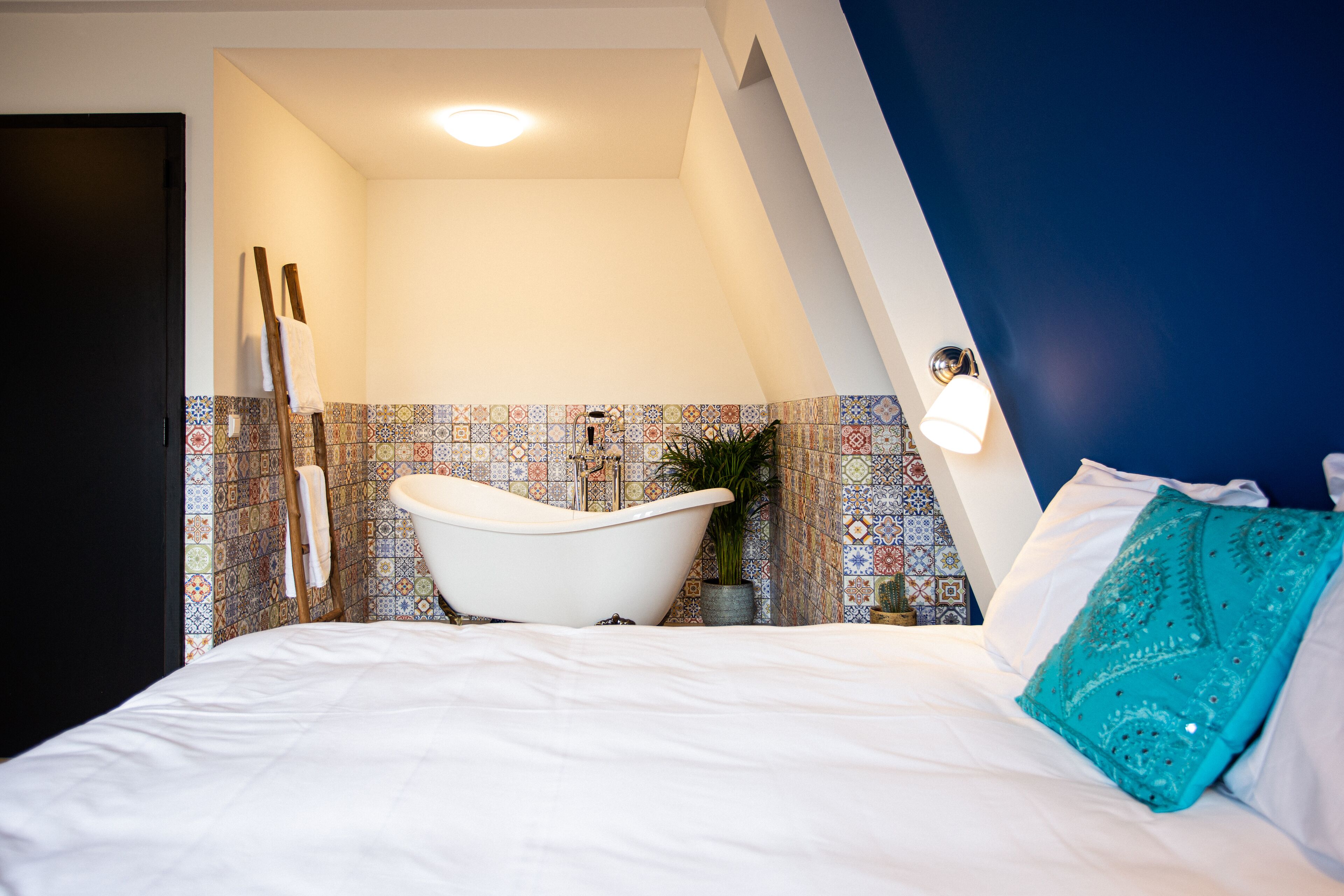 A bedroom with a white bed, a bathtub, and a blue accent wall.