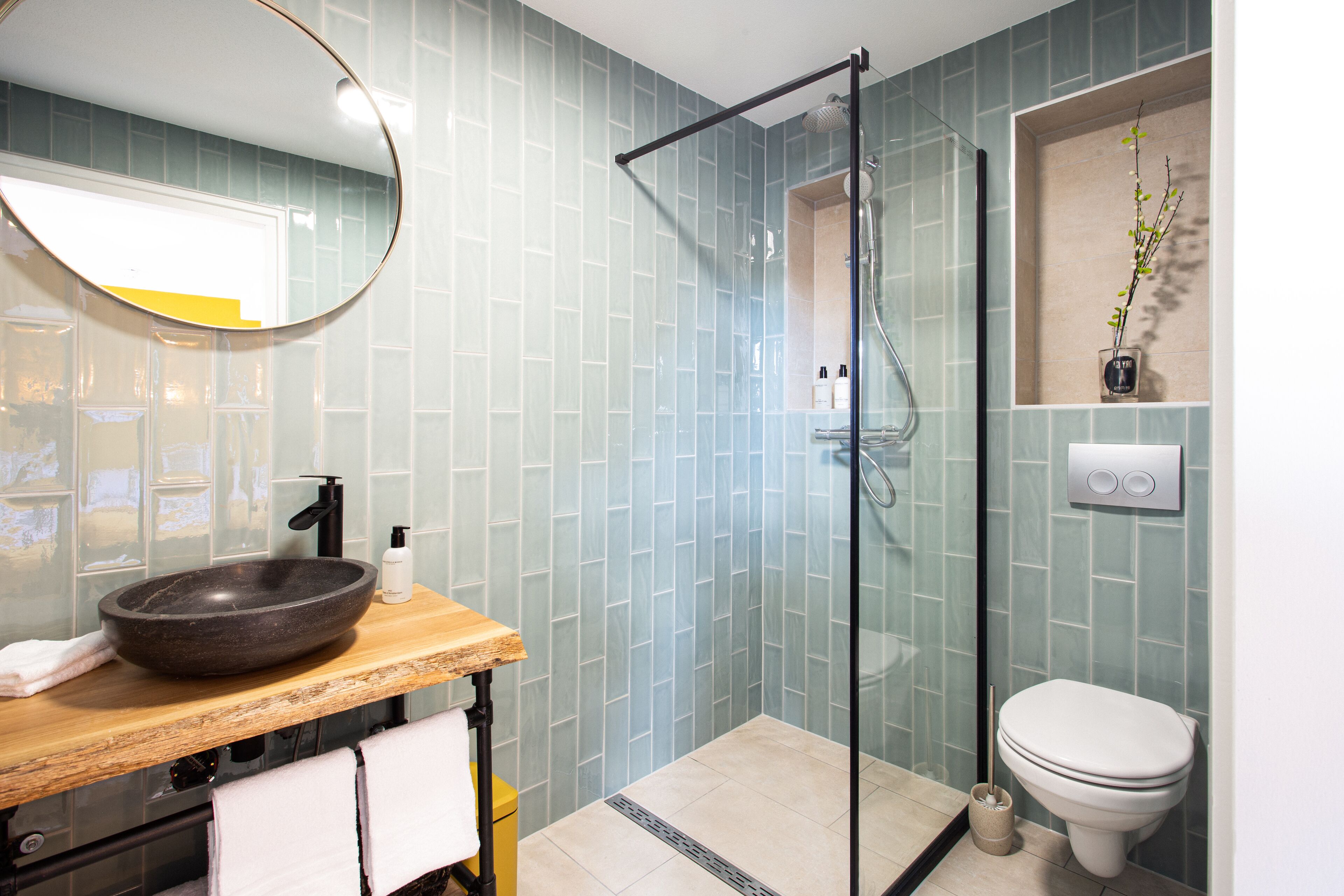 A bathroom with a wooden vanity, a round sink, a glass shower enclosure, and a toilet.