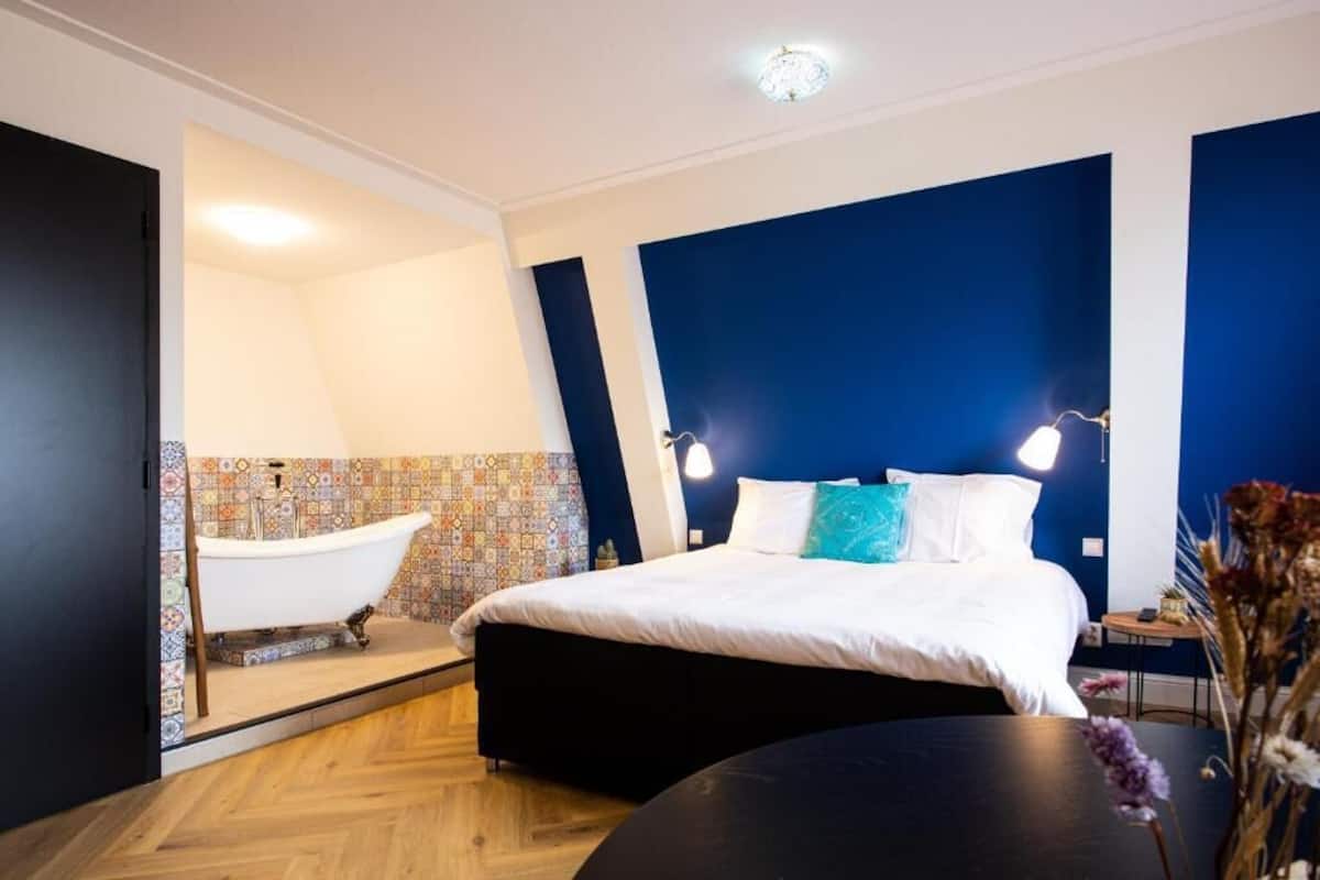 Un dormitorio moderno con una cama grande, una bañera integrada y suelo de madera.