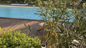 A pool area with a wooden deck, lounge chairs, and lush greenery. - Magnificent new villa between sea and mountains, between Porticcio and Ajaccio (cauro)