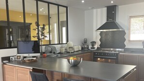 A modern kitchen with a large island, stainless steel appliances, and a black range hood. - Magnificent new villa between sea and mountains, between Porticcio and Ajaccio (cauro)