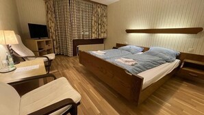 A hotel room with a wooden bed, a desk with a chair, a television, and a window with curtains. - Beny Hotel Restaurant  (Bad Bellingen)