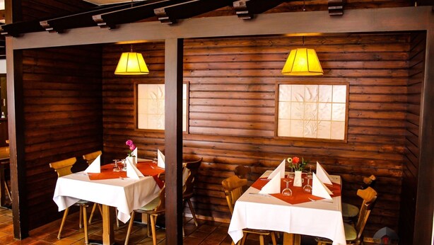 A restaurant with wooden walls, two tables with white tablecloths, and yellow pendant lights. - Beny Hotel Restaurant  (Bad Bellingen)
