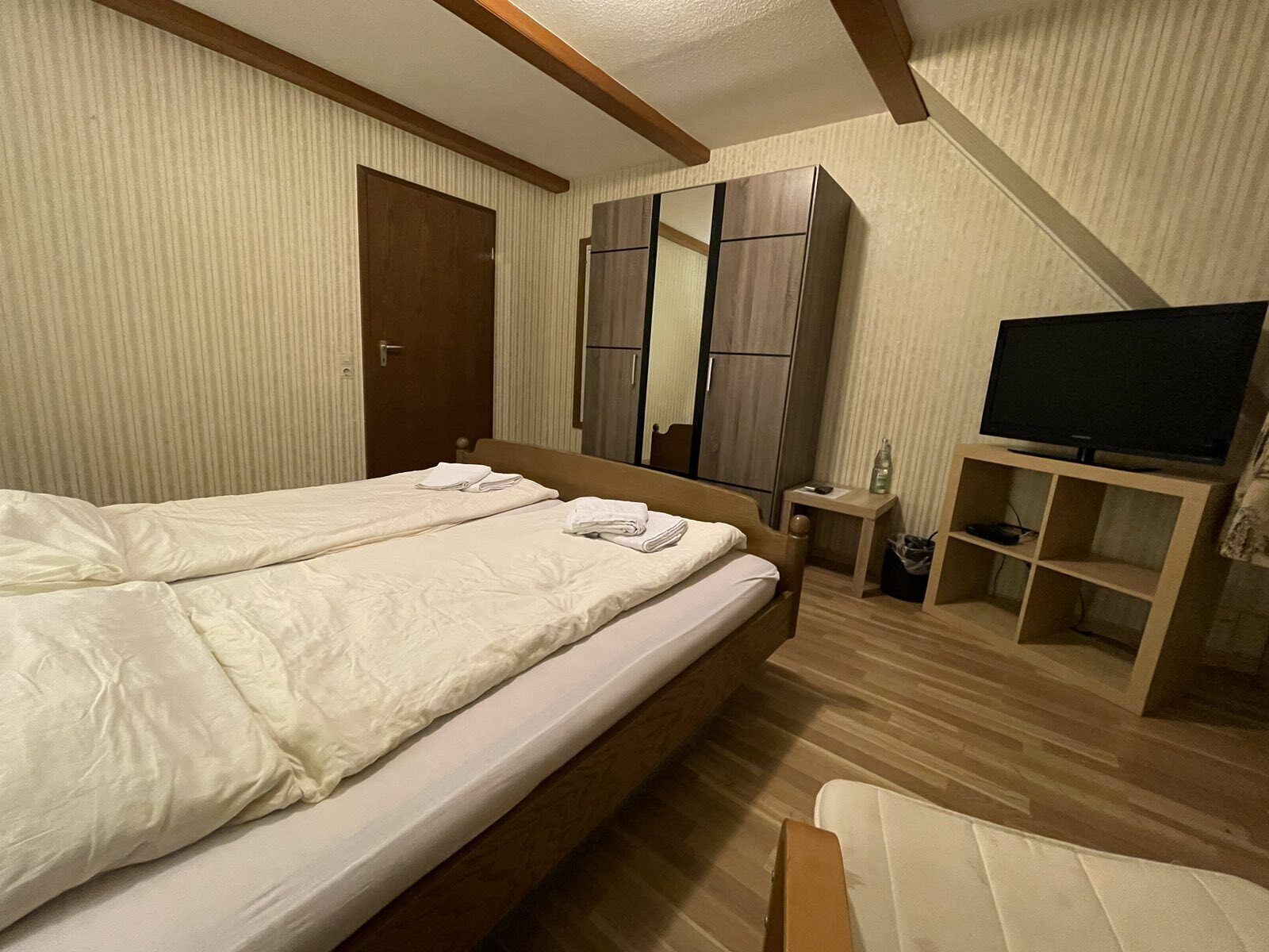 A hotel room with a large bed, a television, a wardrobe, and a small table.