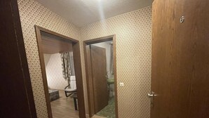 A hallway with patterned wallpaper and wooden flooring, leading to a room with a bed and a chair. - Beny Hotel Restaurant  (Bad Bellingen)