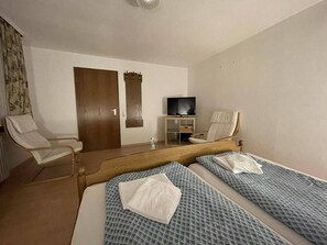 A hotel room with two beds, a TV, a chair, and a wooden door. - Beny Hotel Restaurant  (Bad Bellingen)