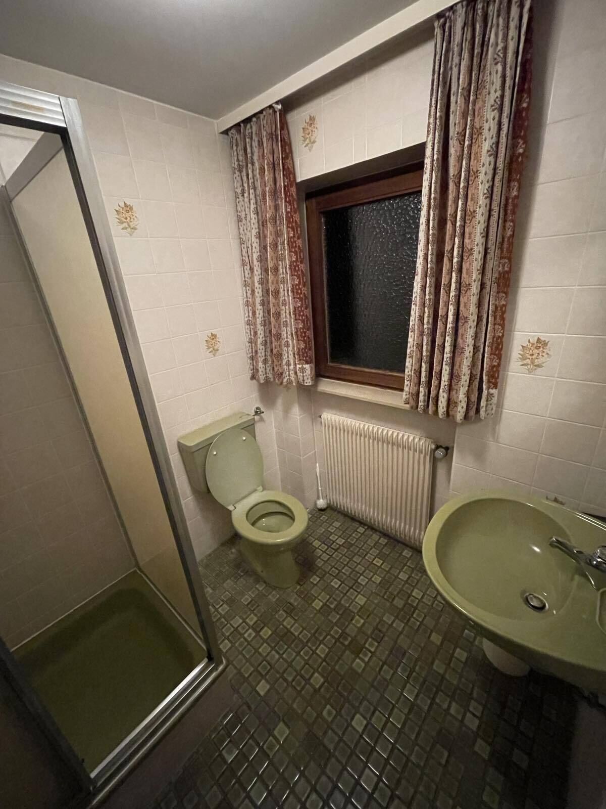 Un baño con inodoro, lavamanos, ventana con cortinas y zona de ducha.