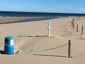 En sandstrand med et hvidt redningspæle og en blå alarmkasse.
