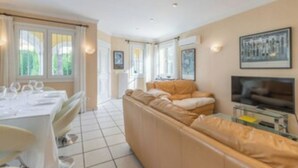 A modern living room with a sofa, a TV, and a dining area with a table and chairs. - Oliva Nova Golf Yellow House (OLIVA)