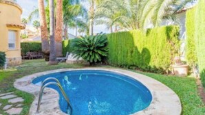 A swimming pool with a stone border, surrounded by a well-maintained lawn and palm trees. - Oliva Nova Golf Yellow House (OLIVA)