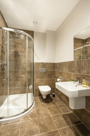 Un baño moderno con cabina de ducha de vidrio, inodoro blanco y lavamanos con artículos de aseo.