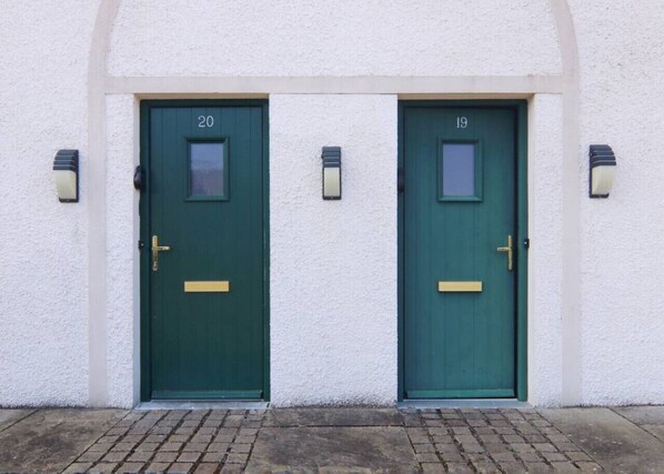 Two green doors with numbers 20 and 19, white textured walls, and small wall-mounted lights.