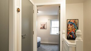 Un pasillo que conduce a un dormitorio con una cama, un ventanal y un cuadro en la pared.