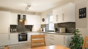 Una cocina moderna con armarios blancos, horno empotrado, microondas y un comedor con mesa y sillas de madera.