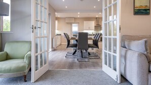An open-plan living and dining area with a kitchen, a green armchair, a grey sofa, and a dining table with chairs. - 12b Crest Rd · Escape Ordinary in Enniskillen (Enniskillen)