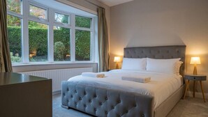 A bedroom with a large bed, two bedside tables with lamps, a radiator, and a window with curtains. - 12b Crest Rd · Escape Ordinary in Enniskillen (Enniskillen)