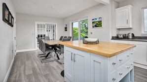 A modern kitchen with a wooden island, white cabinetry, and a dining area with grey chairs. - 12b Crest Rd · Escape Ordinary in Enniskillen (Enniskillen)