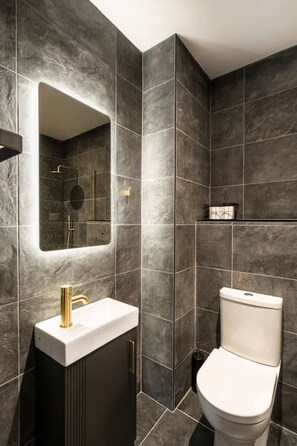 Un baño moderno con baldosas oscuras, un grifo dorado y un inodoro blanco.