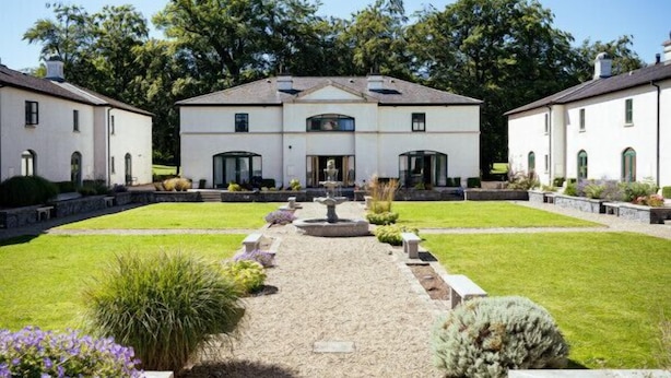 A symmetrical building with a central entrance, surrounded by a well-maintained lawn and garden beds.