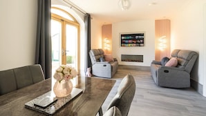 A modern living room with a fireplace, two grey sofas, a coffee table with a vase of flowers, and a TV mounted on the wall.