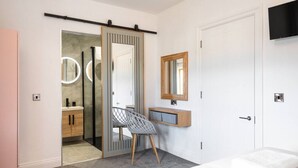 A bedroom with a bed, a desk with a chair, a mirror, and a sliding door leading to a bathroom.