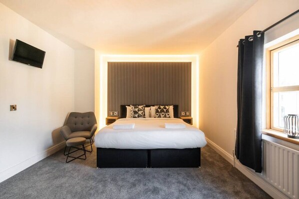 Habitación de hotel con una cama grande, una silla, un televisor y una ventana con cortinas.