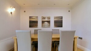 Un coin repas avec une table en bois et quatre chaises, trois tableaux accrochés au-dessus de la table et un luminaire fixé au mur.