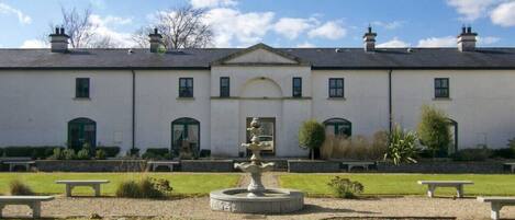 A building with a symmetrical facade, a central arched entrance, and a circular fountain in the courtyard.