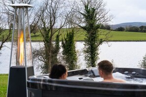 A hot tub with two people, a lamp post, and a lake view.