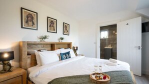 Un letto rifatto con cuscini, un comodino con una lampada e un vassoio con snack e bicchieri sul letto.