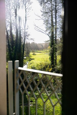 A view through a lattice fence with a grassy field and trees in the background. - 60 Lough Erne Golf Village · Escape Ordinary at Lough Erne! (Castle Hume/Lough Erne)