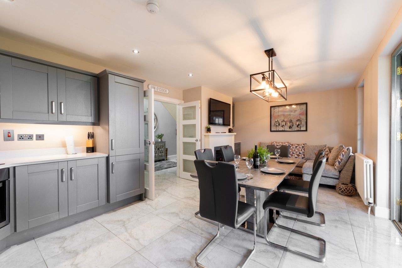 A modern kitchen with grey cabinets, a dining area with a table and chairs, and a living space with a sofa and a television.