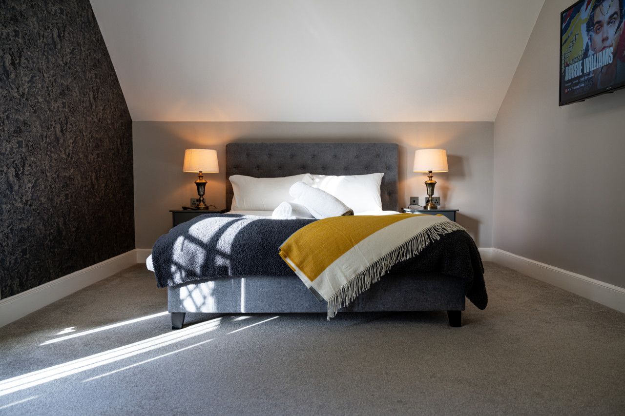 A bedroom with a bed, two bedside lamps, a throw blanket, and a wall-mounted TV.