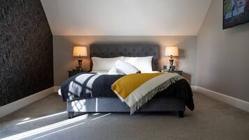 A bedroom with a bed, two bedside lamps, a throw blanket, and a wall-mounted TV.
