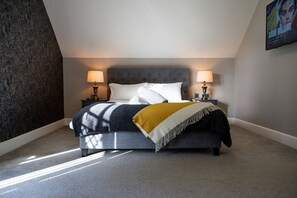 A bedroom with a bed, two bedside lamps, a throw blanket, and a wall-mounted TV.