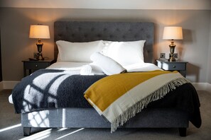 A bed with a grey upholstered headboard, white pillows, a mustard-colored throw blanket, and two bedside lamps on matching nightstands. - 60 Lough Erne Golf Village · Escape Ordinary at Lough Erne! (Castle Hume/Lough Erne)