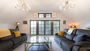 A modern living room with two dark grey sofas, a glass coffee table, and a chandelier. - 60 Lough Erne Golf Village · Escape Ordinary at Lough Erne! (Castle Hume/Lough Erne)