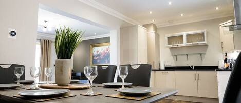 A dining area with a table set for four, a potted plant, and a painting on the wall.