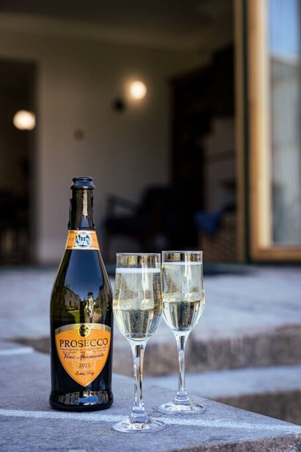 Une bouteille de prosecco et deux verres posés sur une surface en pierre.