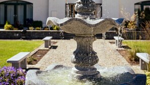 A stone fountain with water flowing, set in a landscaped garden with benches and a building in the background. - LE 23 · Escape Ordinary at Castle Hume No.23 ~ Luxury (Fermanagh and Omagh)