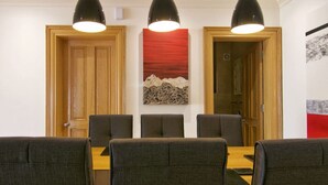 Un coin repas avec une table en bois et six chaises, trois lampes suspendues au-dessus, et un tableau abstrait rouge accroché au mur.