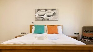 Un lit bien fait, avec du linge de lit blanc et deux oreillers, une tête de lit en bois et un tableau représentant des fleurs accroché au mur.