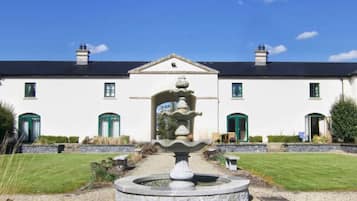 A white building with a symmetrical facade, a central fountain, and a well-maintained lawn.