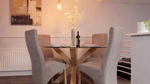 Een eettafel met vier grijze gestoffeerde stoelen, een fles wijn en een vaas met bloemen.