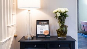 A black console table with a white lamp, a framed welcome sign, and a vase of white flowers.
