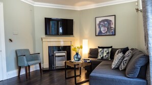 A living room with a sofa, armchair, fireplace, flat-screen TV, and artwork on the wall.